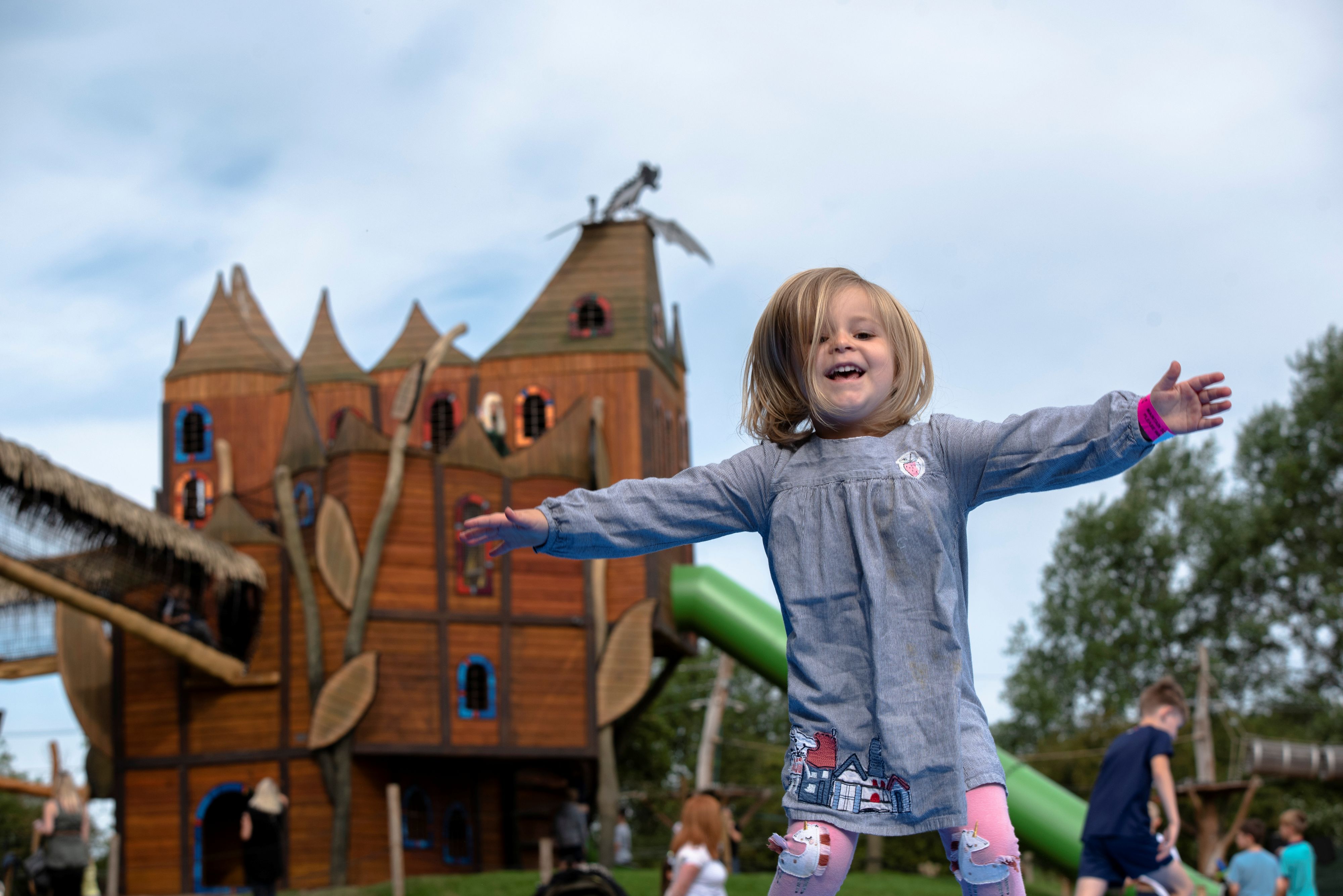 Toddler playing with arms outstretched in front of an adventure playground tower at Hobbledown