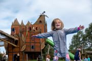 Toddler playing with arms outstretched in front of an adventure playground tower at Hobbledown